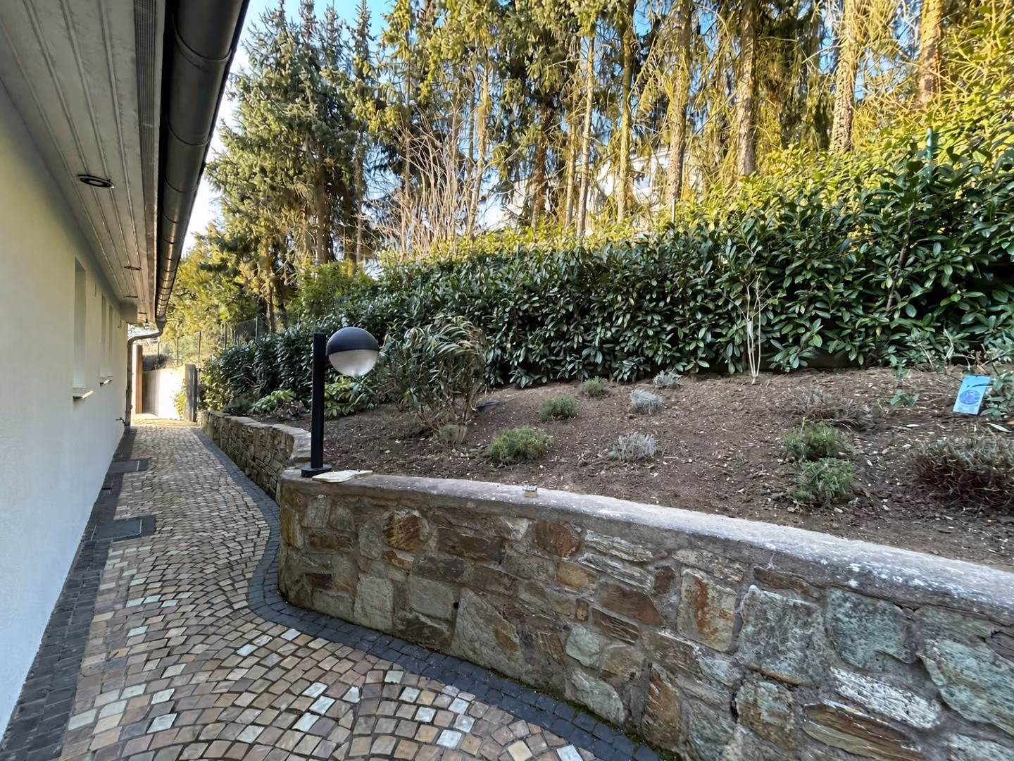 Pflasterweg, Natursteinmauer und hohe Hecke an einem von Birnbaum betreuten Objekt